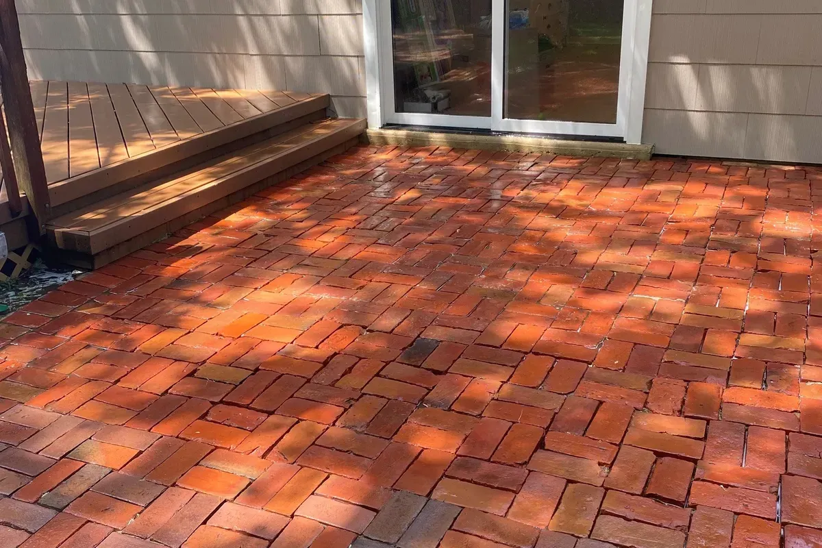 Red brick patio with wooden steps leading to a sliding glass door.
