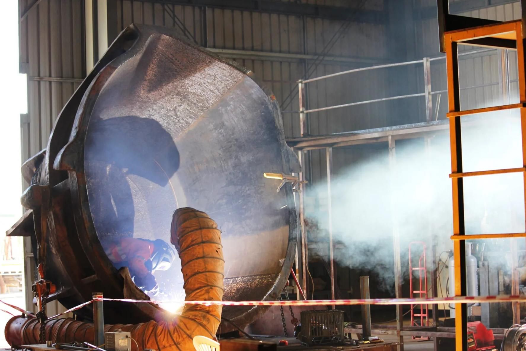 A Man Is Welding A Large Piece Of Metal In A Factory — HardRok Engineering Pty Ltd In Mount Isa, QLD