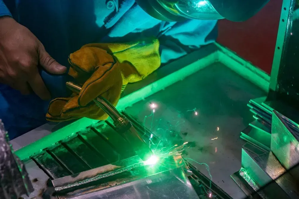 A Man Is Welding A Piece Of Metal With A Green Light Behind Him — HardRok Engineering Pty Ltd In Mount Isa, QLD
