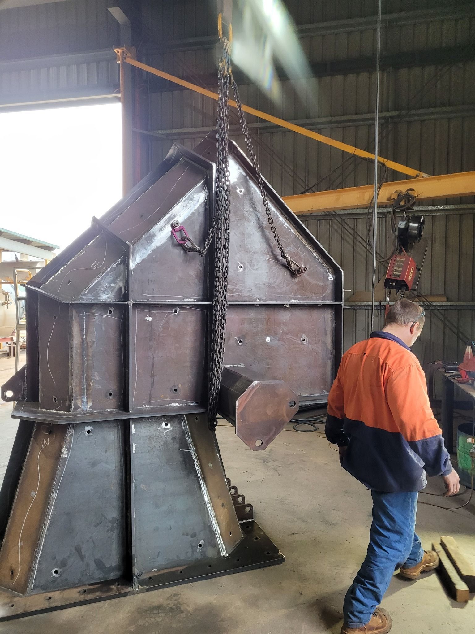 A Man Is Standing Next To A Large Metal Structure Being Lifted By A Crane — HardRok Engineering Pty Ltd In Mount Isa, QLD