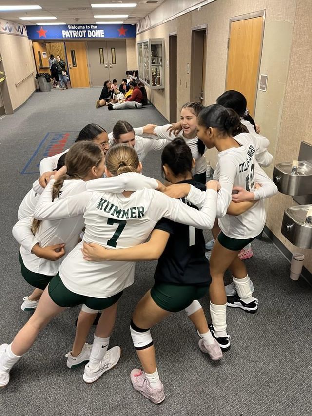 Volleyball team huddles in a hallway, arms around each other before a game.