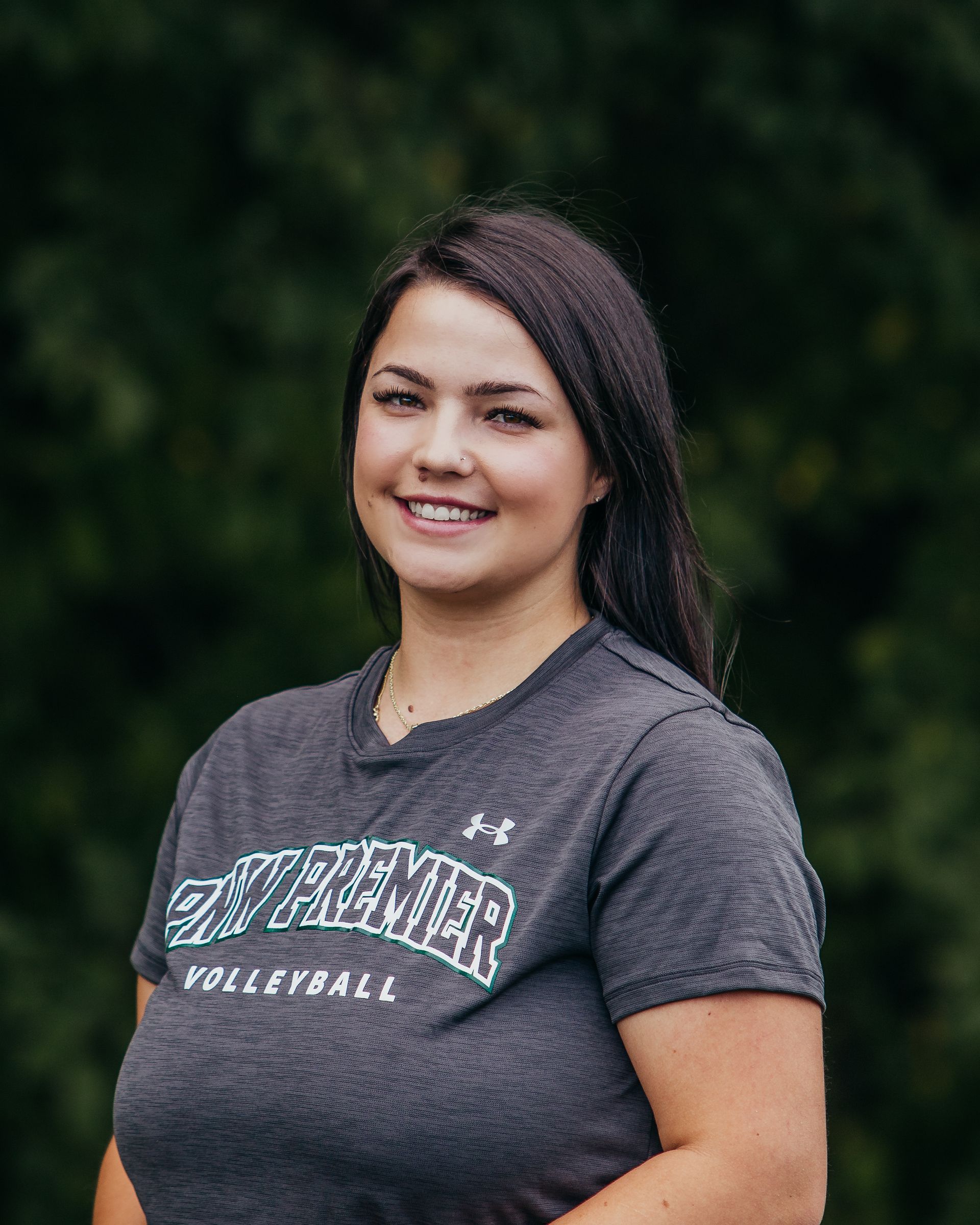 Woman smiling outdoors in a gray Westmont Volleyball T-shirt against a dark green background