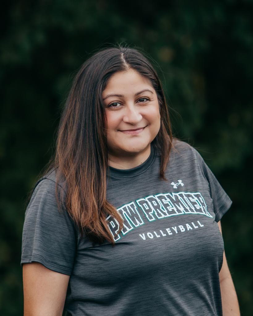 Smiling student in a dark gray volleyball T-shirt against a blurred green background