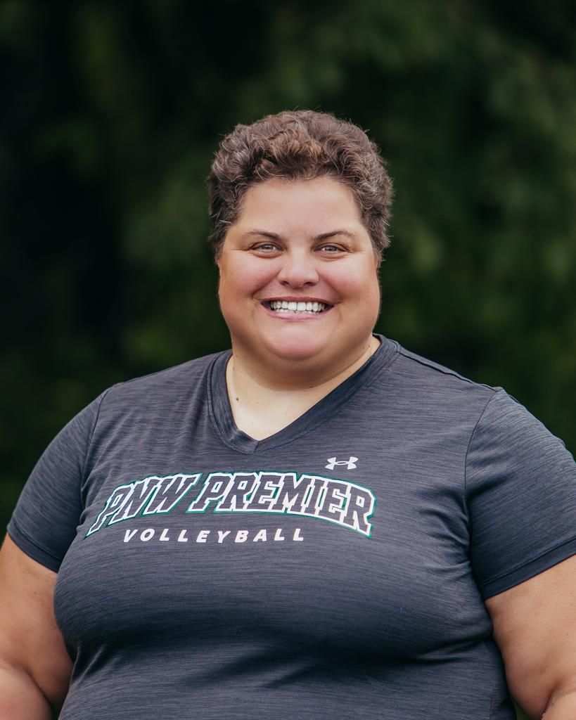 Smiling person in a gray Premier Volleyball T-shirt against a blurred green outdoor background