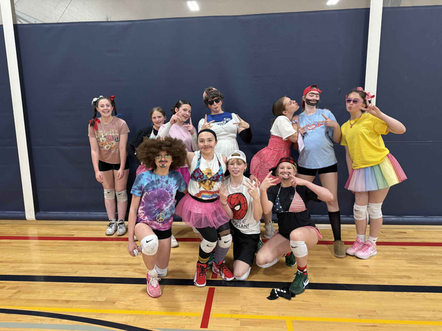 Group of dancers posing on a gym floor in colorful outfits, smiling in a studio-like setting