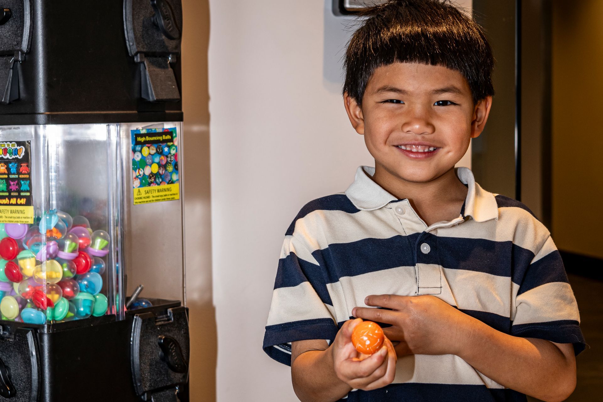 A young boy is holding an orange in front of a gumball machine.