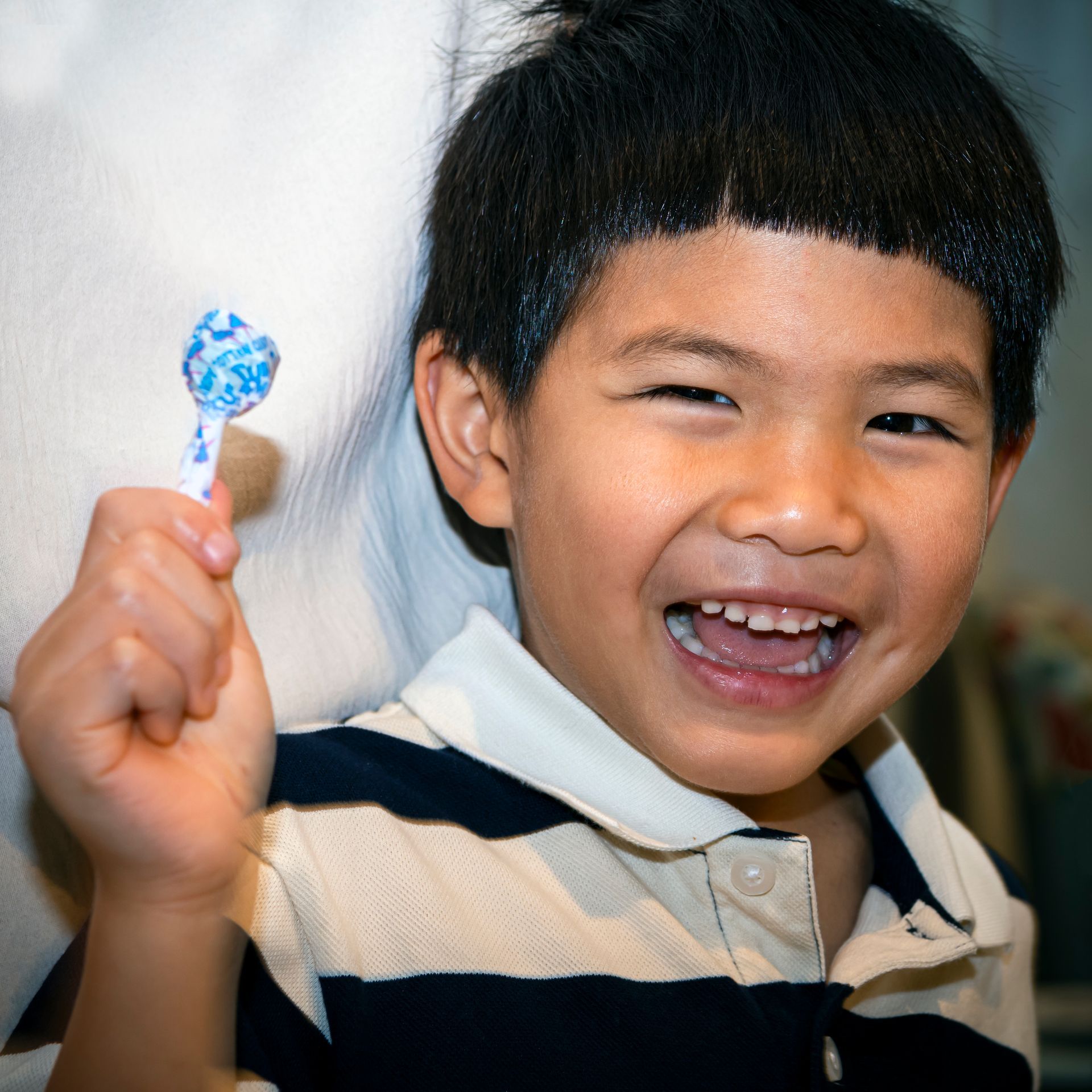 A young boy is smiling while holding a blue lollipop