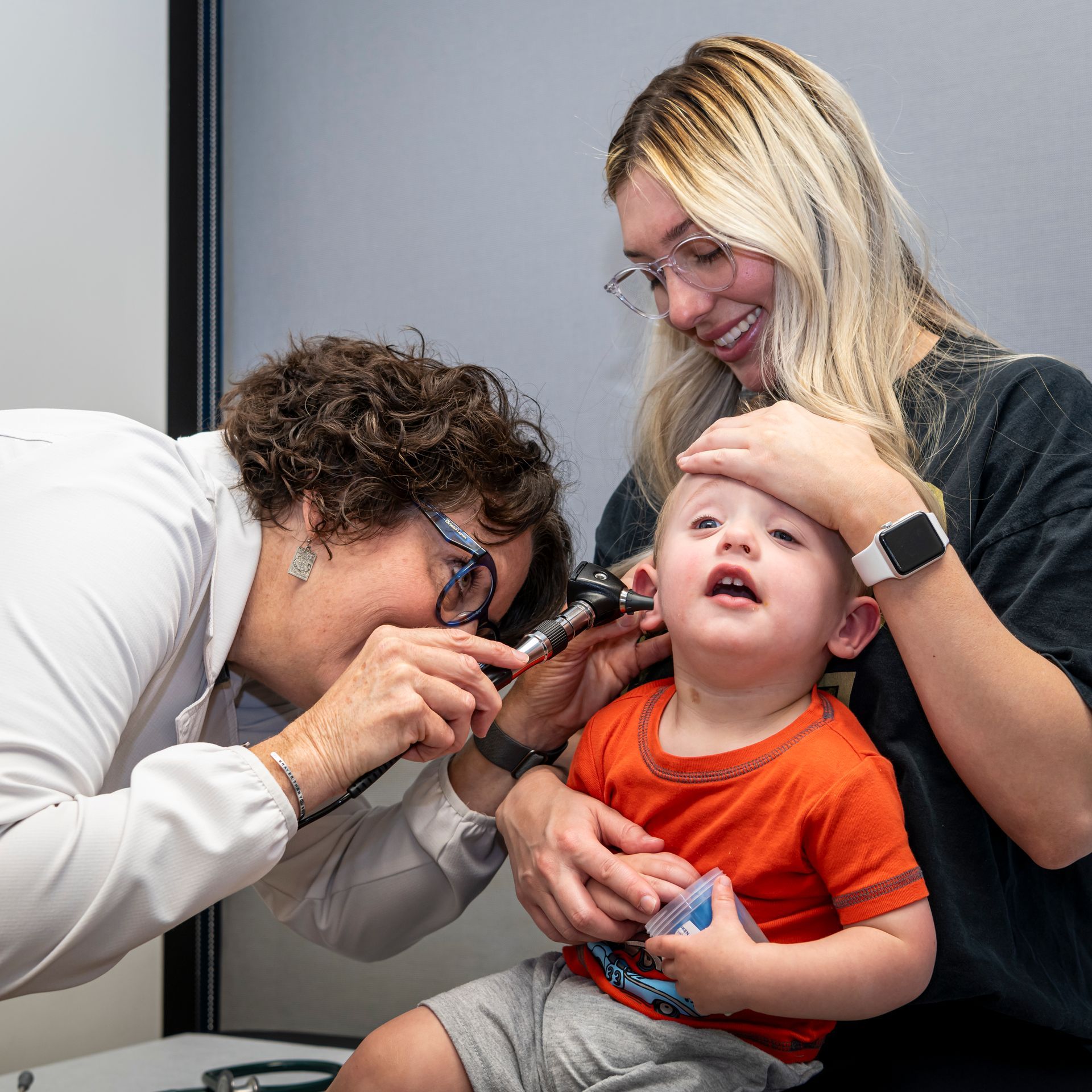 Pediatrician looking into the ears of a child while his parent watches