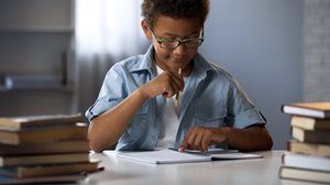 A young boy is sitting at a table with a stack of books.