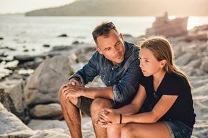 A man and a girl are sitting on the beach talking to each other.