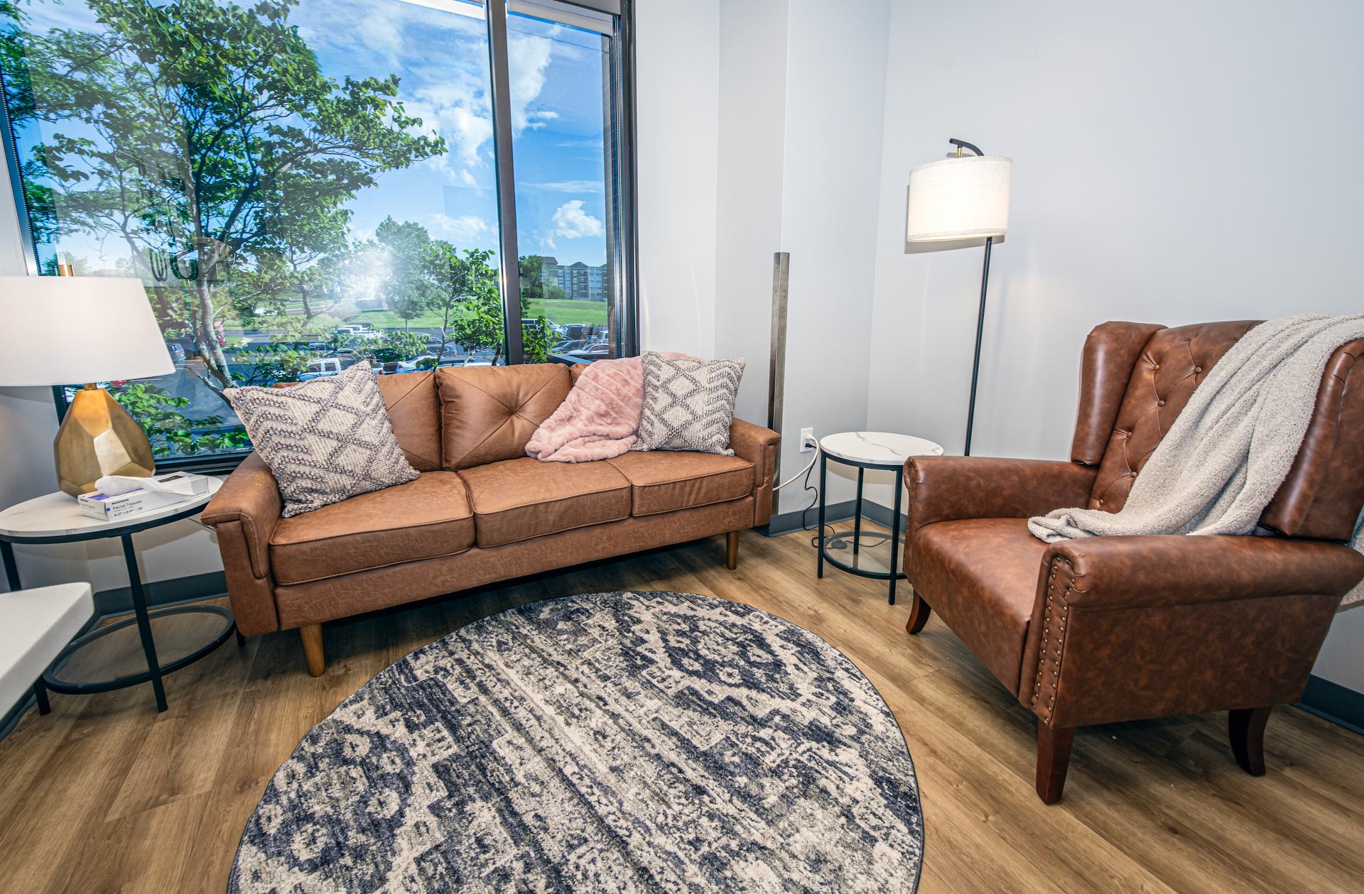 A comfortable therapy room with a couch , chair , table and rug.