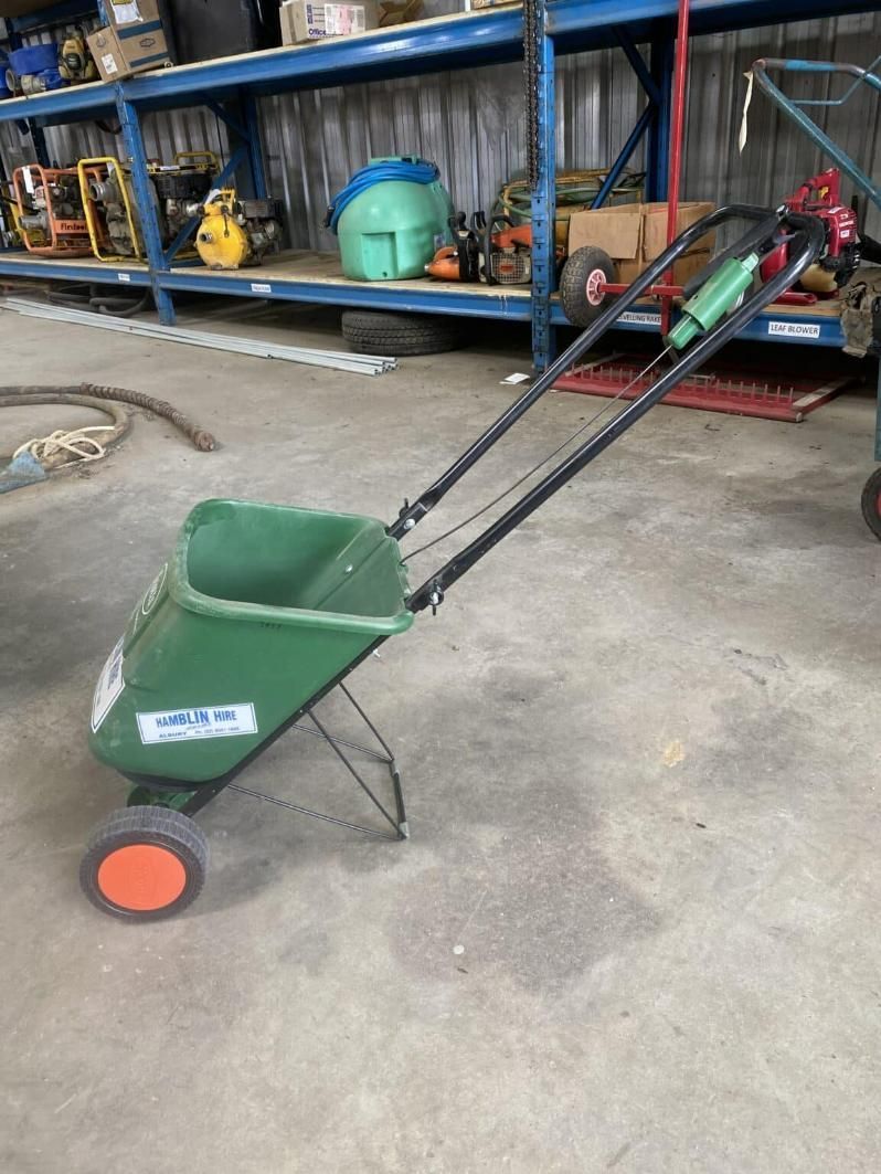 A Green Wheelbarrow With Orange Wheels is Sitting on the Floor in a Warehouse — Hamblin Hire in Albury, NSW