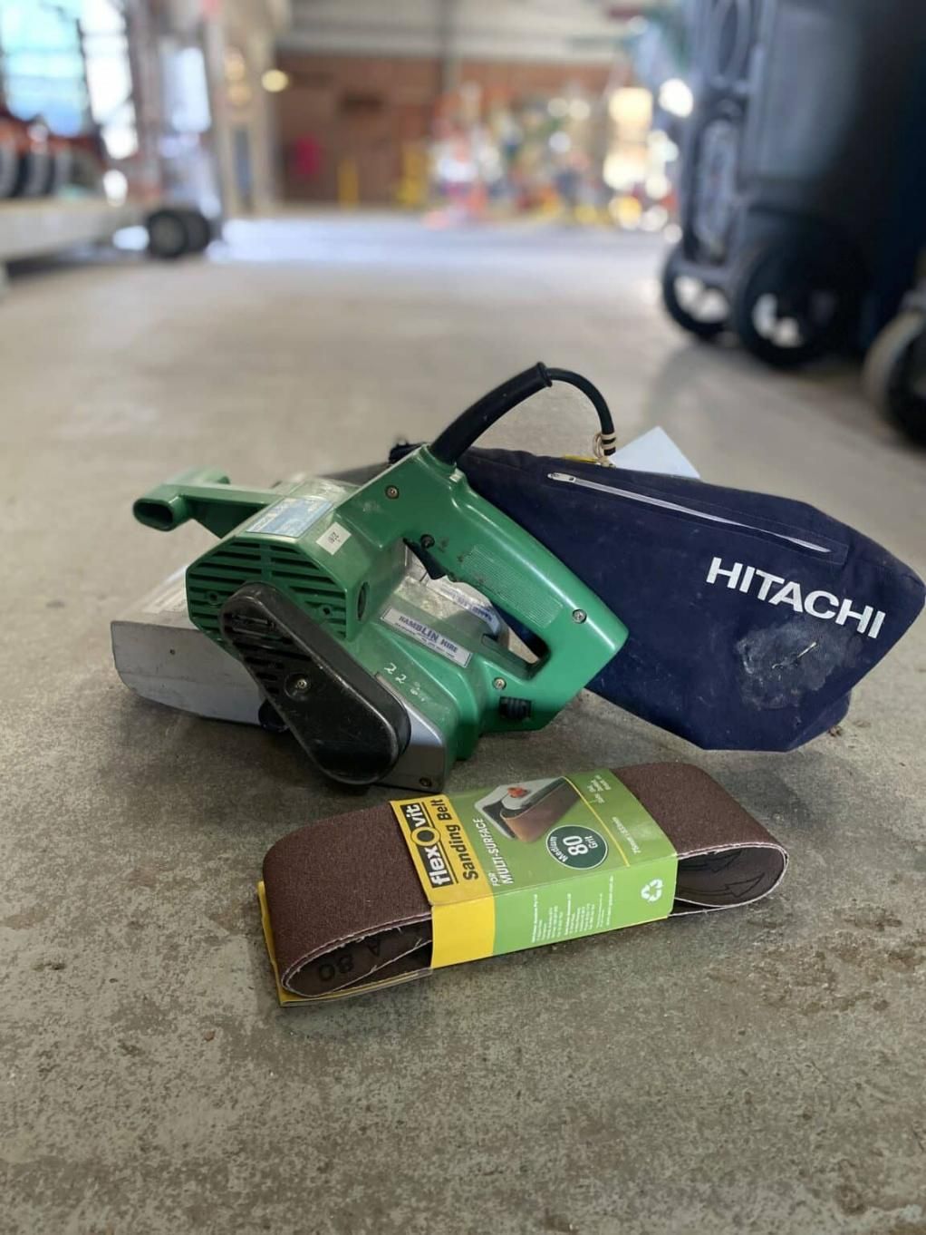 A Hitachi Belt Sander is Sitting on the Floor Next to a Sanding Belt — Hamblin Hire in Albury, NSW