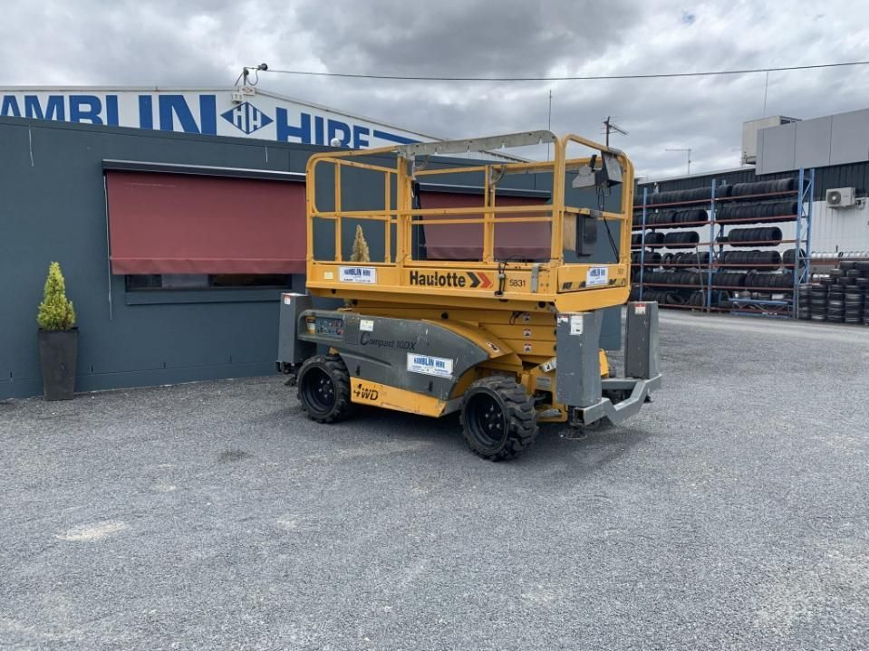 A Yellow Scissor Lift is Parked in Front of a Building — Hamblin Hire in Albury, NSW