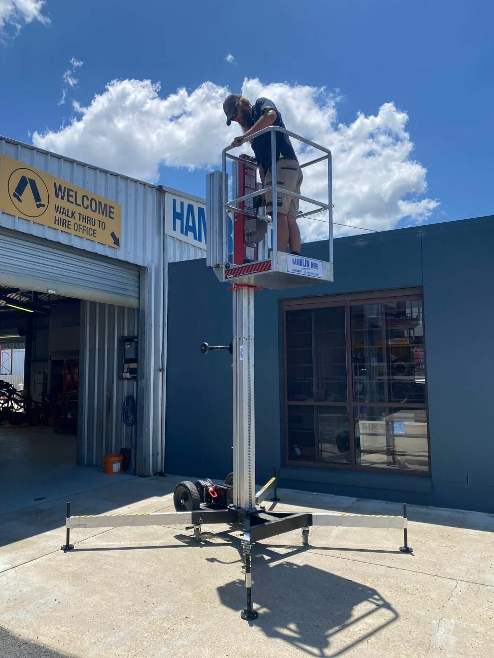 A Man is Standing on a Lift in Front of a Building — Hamblin Hire in Albury, NSW