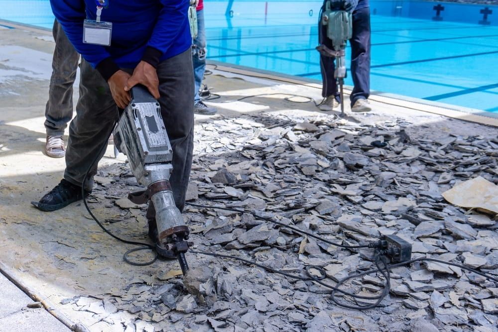 A Man is Using a Hammer to Break Up Concrete Next to a Swimming Pool — Hamblin Hire in Albury, NSW