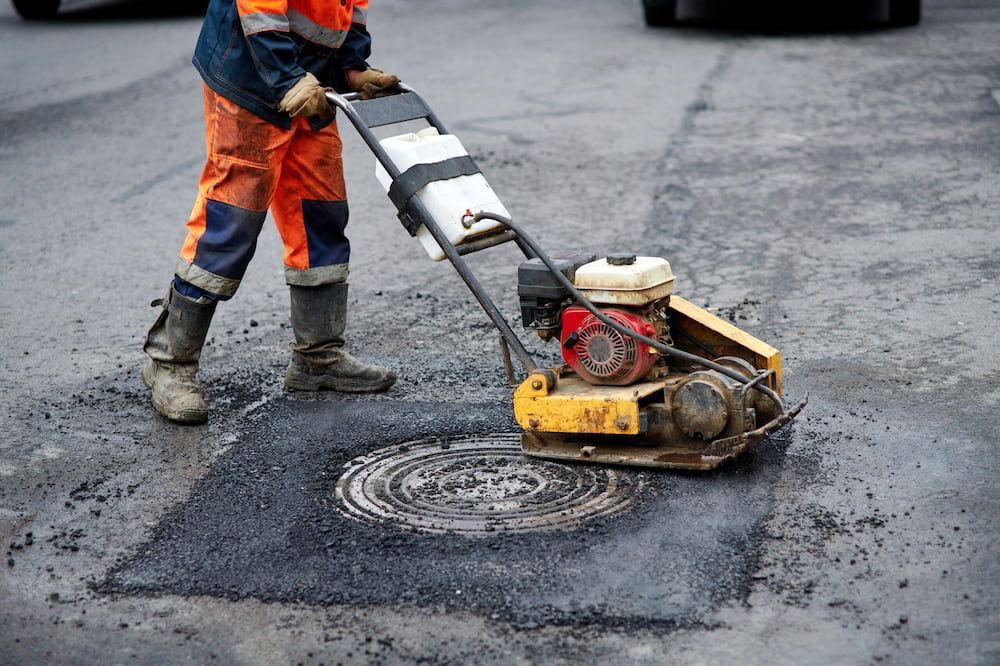 A Man is Using a Machine to Fix a Manhole Cover on the Road — Hamblin Hire in Albury, NSW