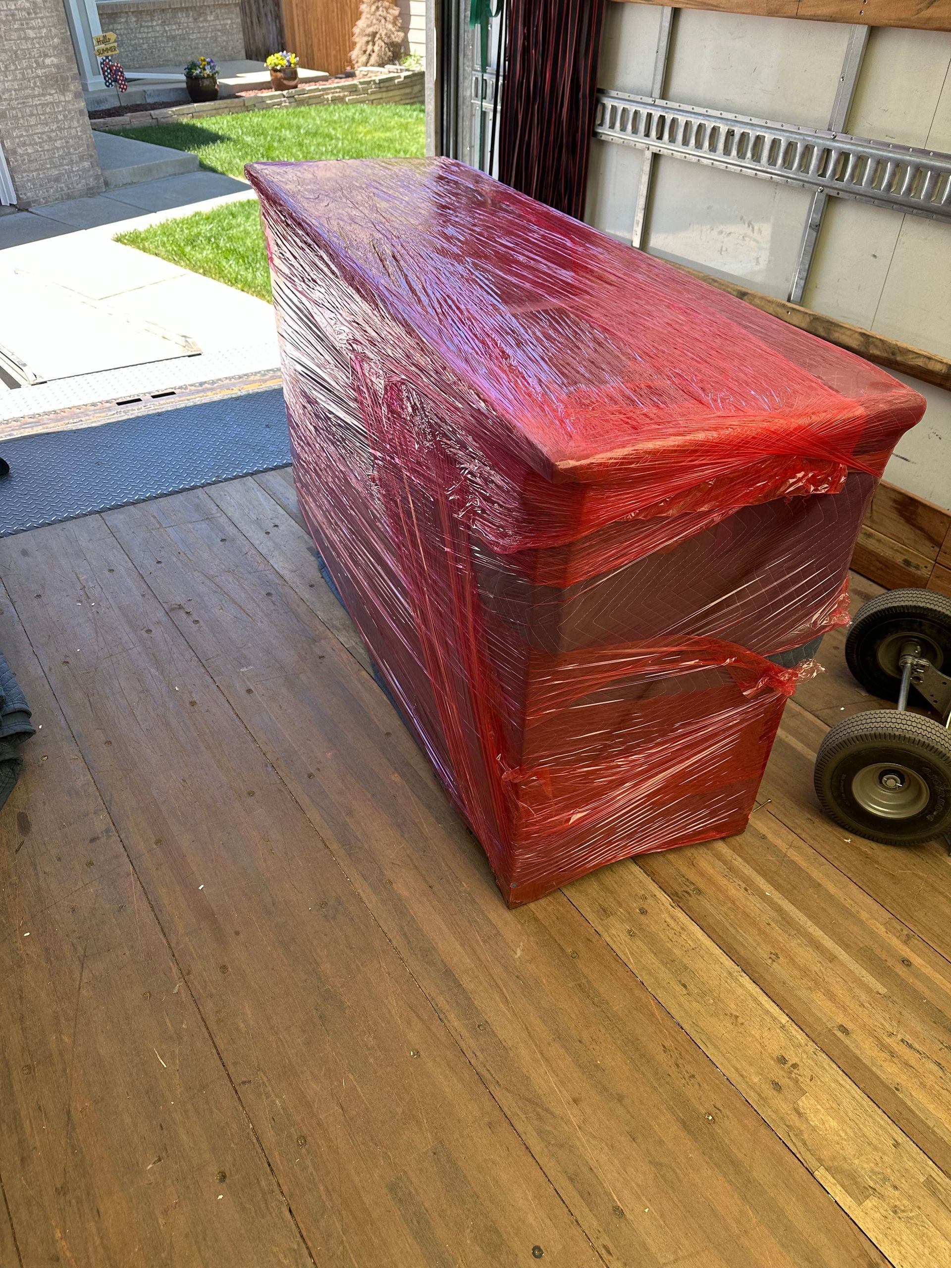 A large, wrapped piece of furniture covered in red bubble wrap sits in the back of a truck.