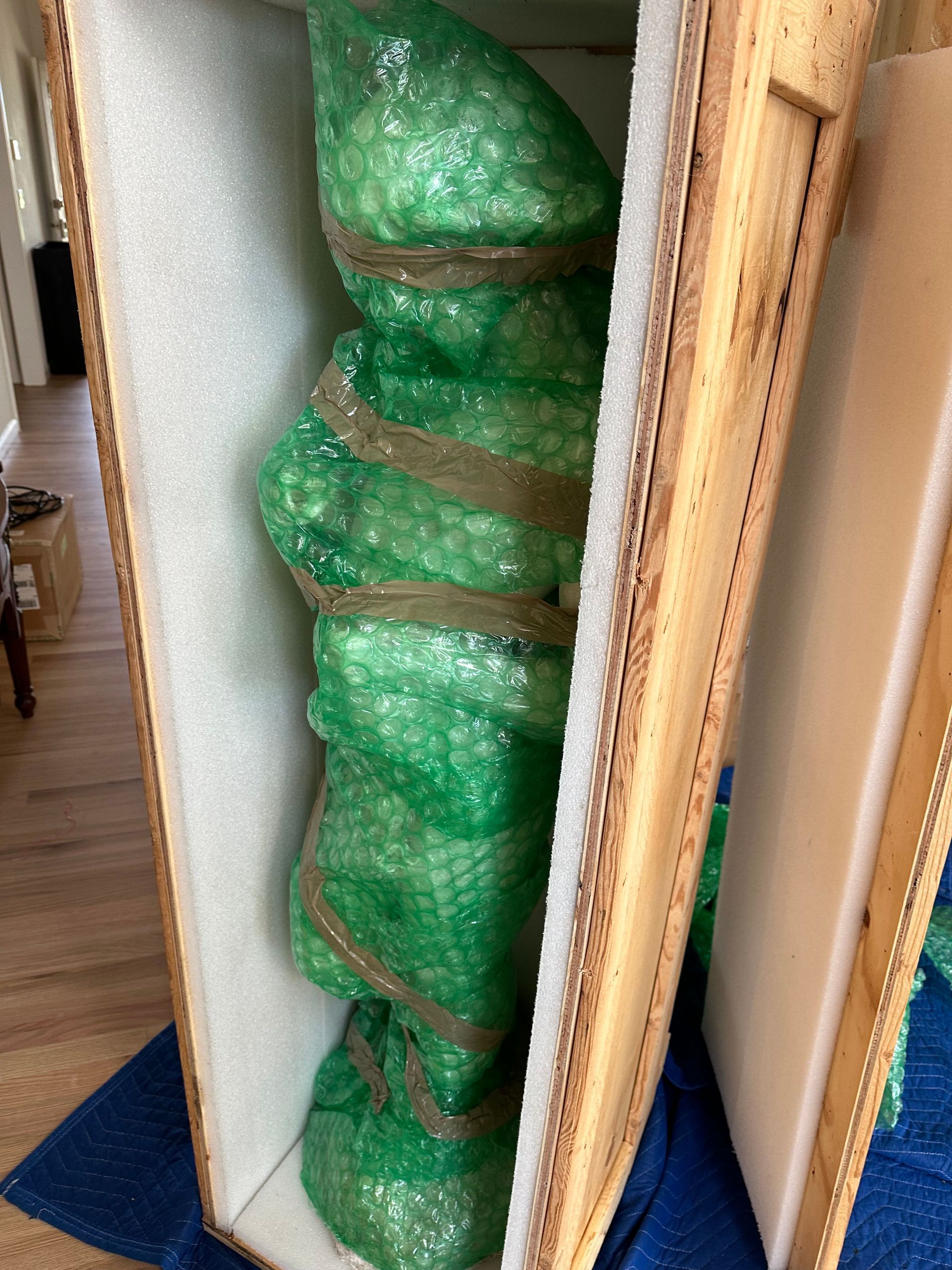 A green-wrapped sculpture secured inside a wooden crate with foam padding.