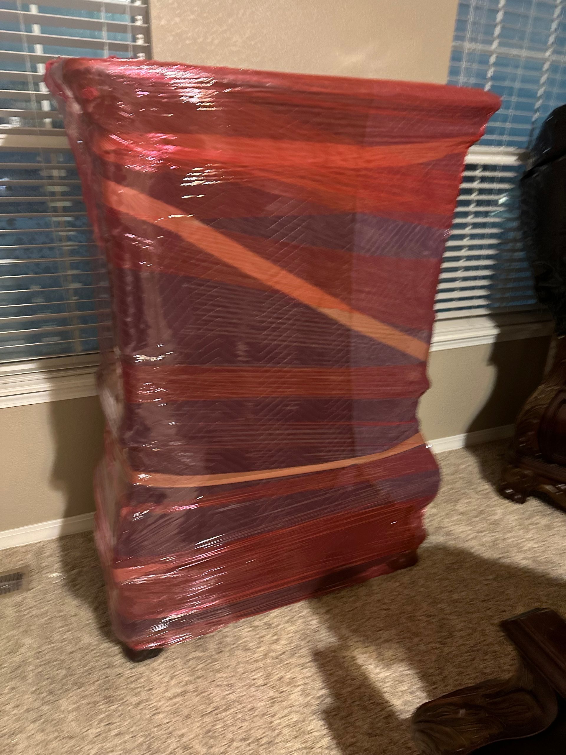 A tall, ornate piece of furniture wrapped in red bubble wrap stands in front of a window.