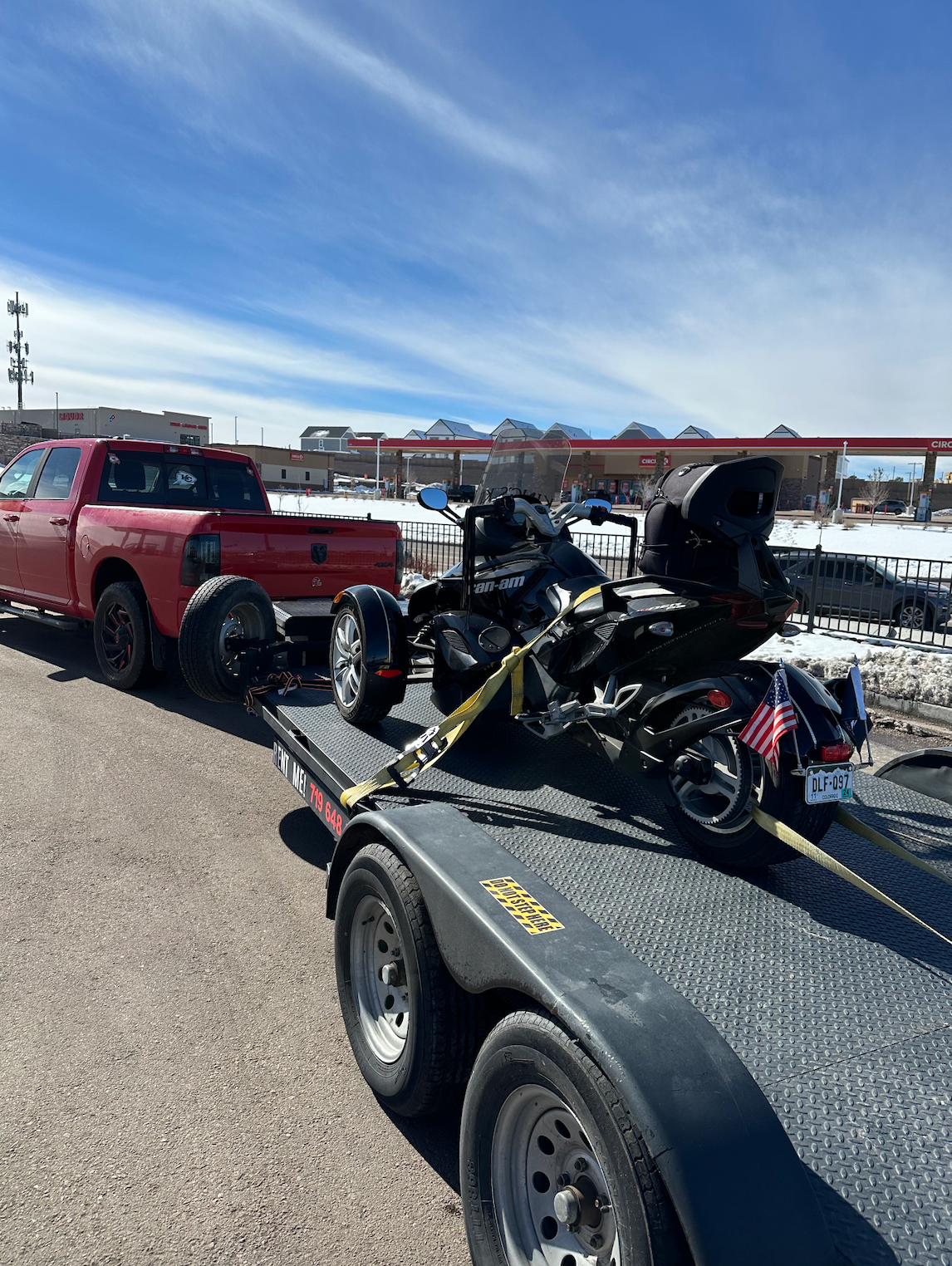 A red truck is towing a snowmobile on a trailer.