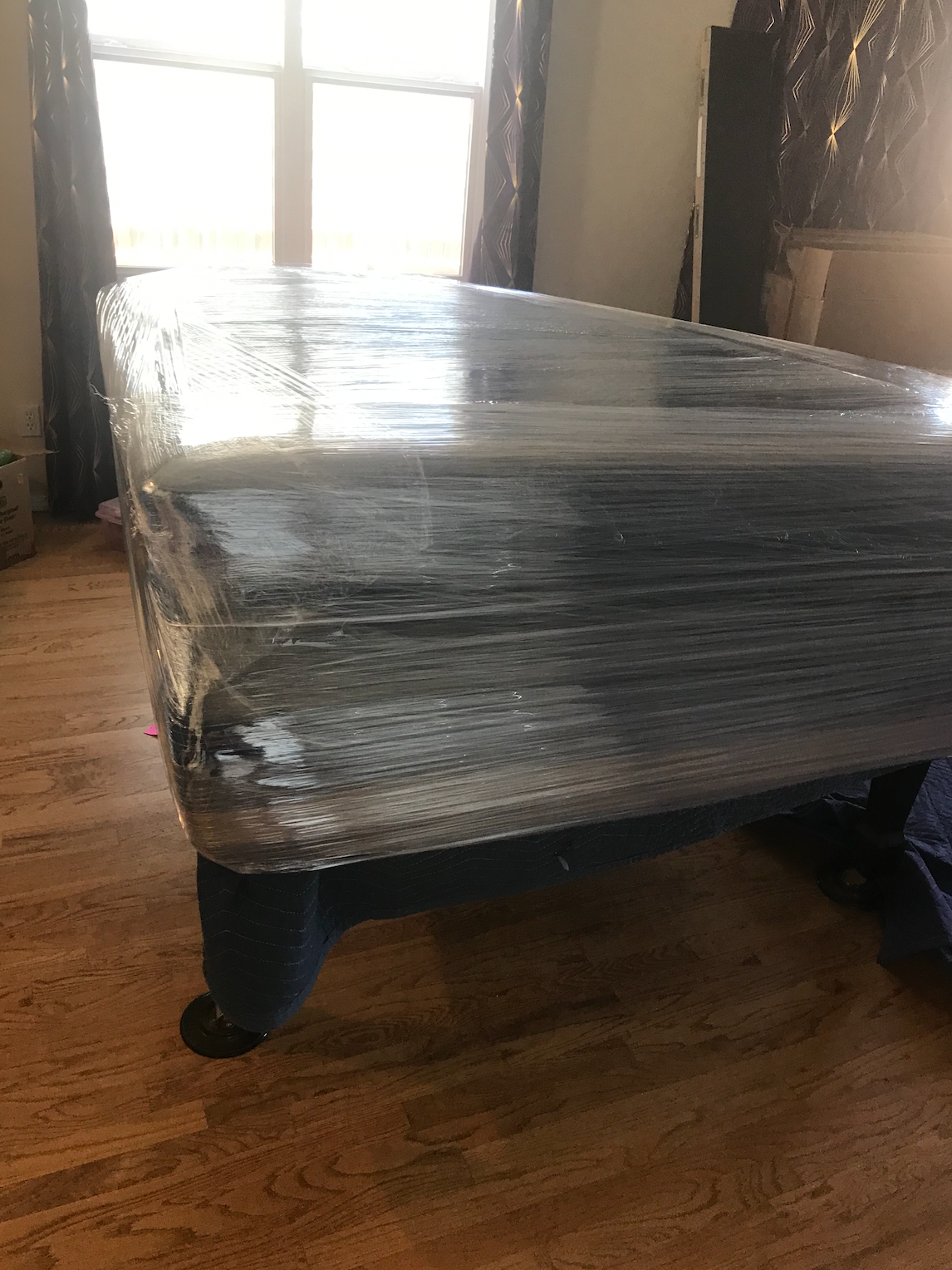 A pool table is wrapped in plastic wrap in a living room.