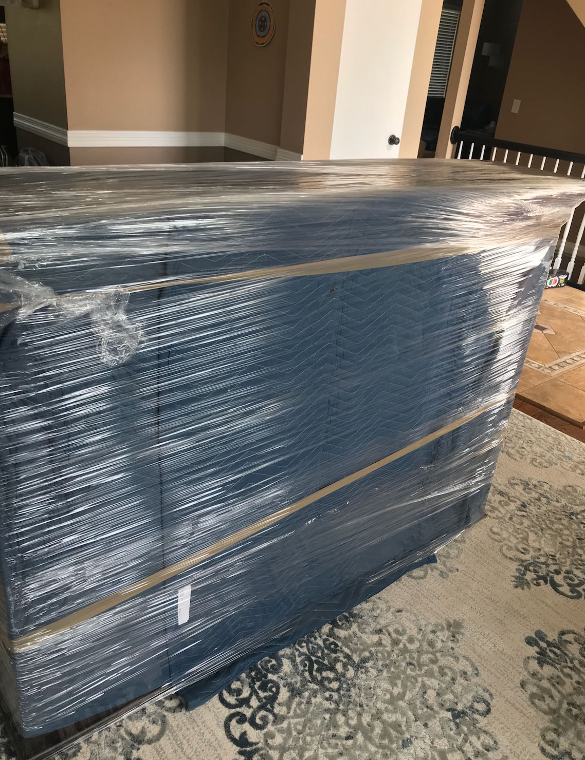 A piano is wrapped in plastic wrap in a living room.