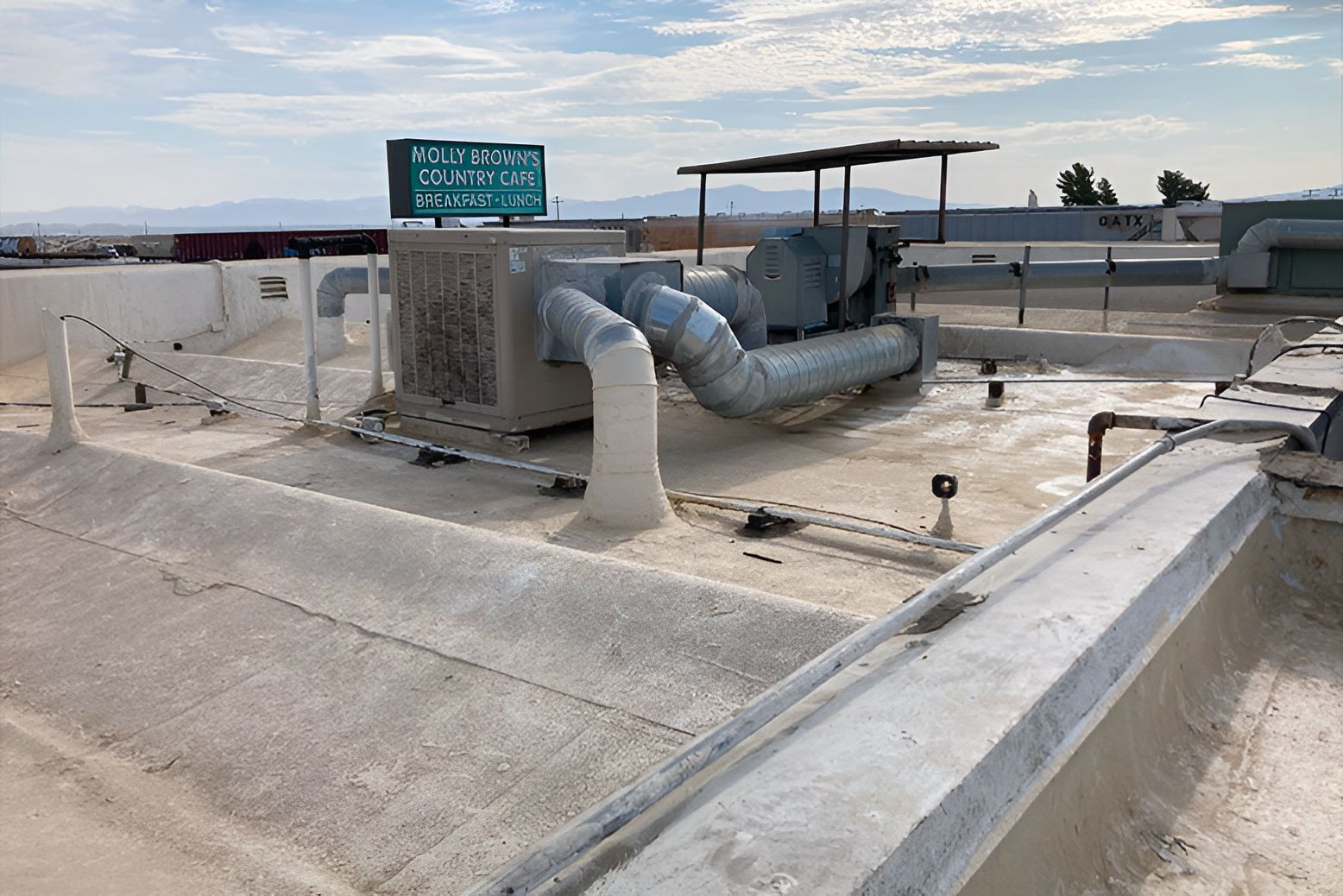 Rooftop HVAC equipment on a white coated roof; ductwork, a sign, and a distant mountain range.