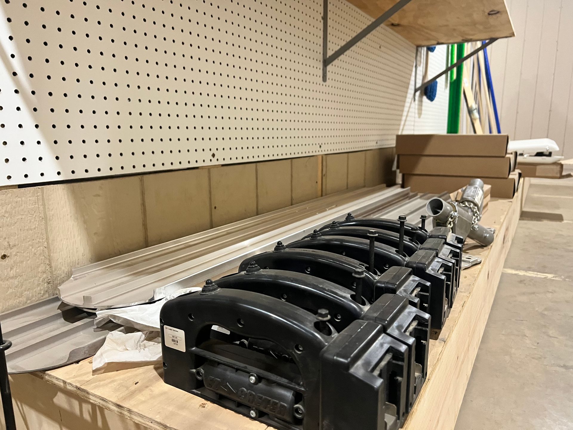 Black automotive parts and silver rails on a wooden surface in a workshop.