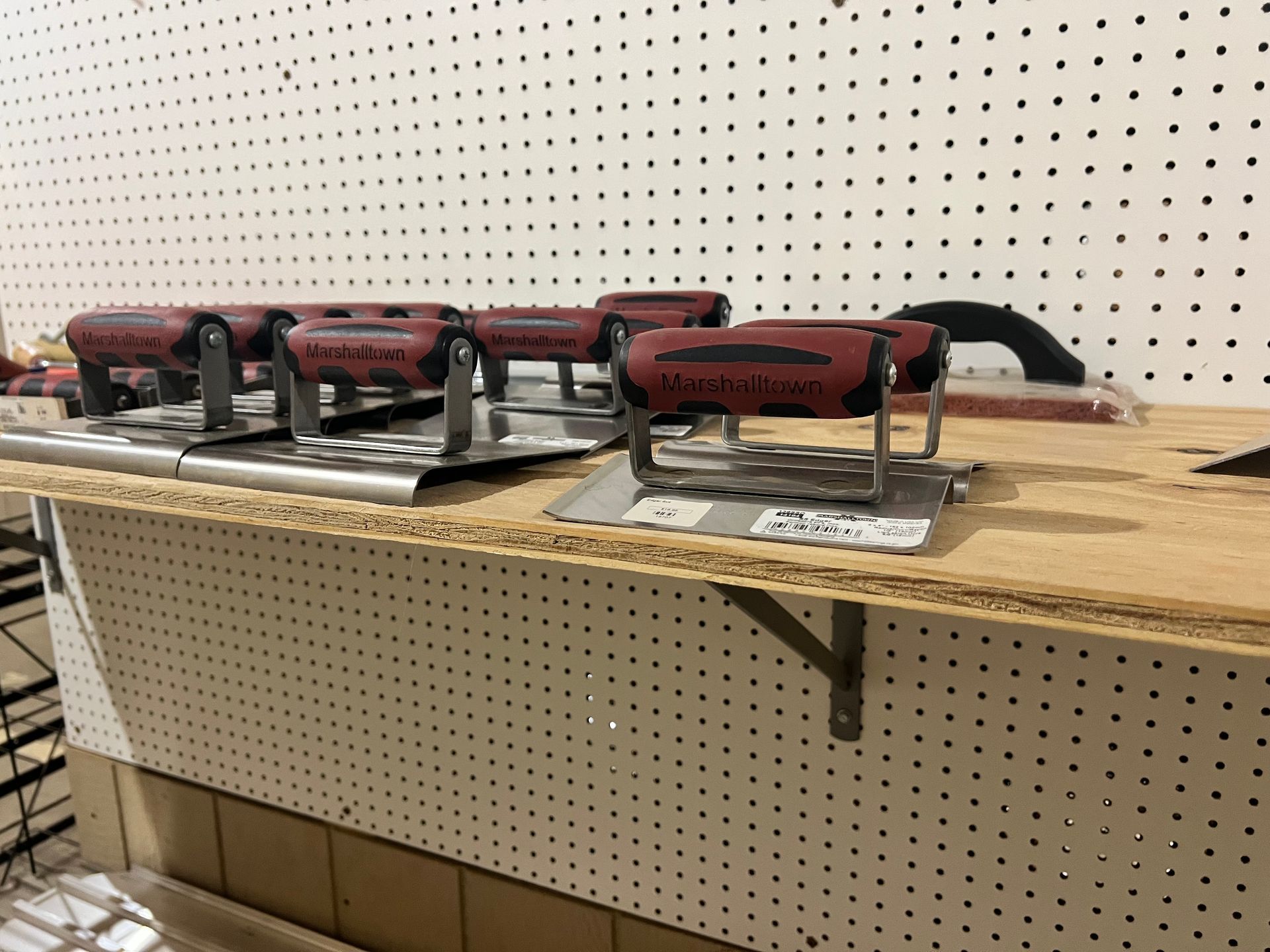 Concrete finishing tools on a shelf in front of pegboard. Red handles, stainless steel blades.