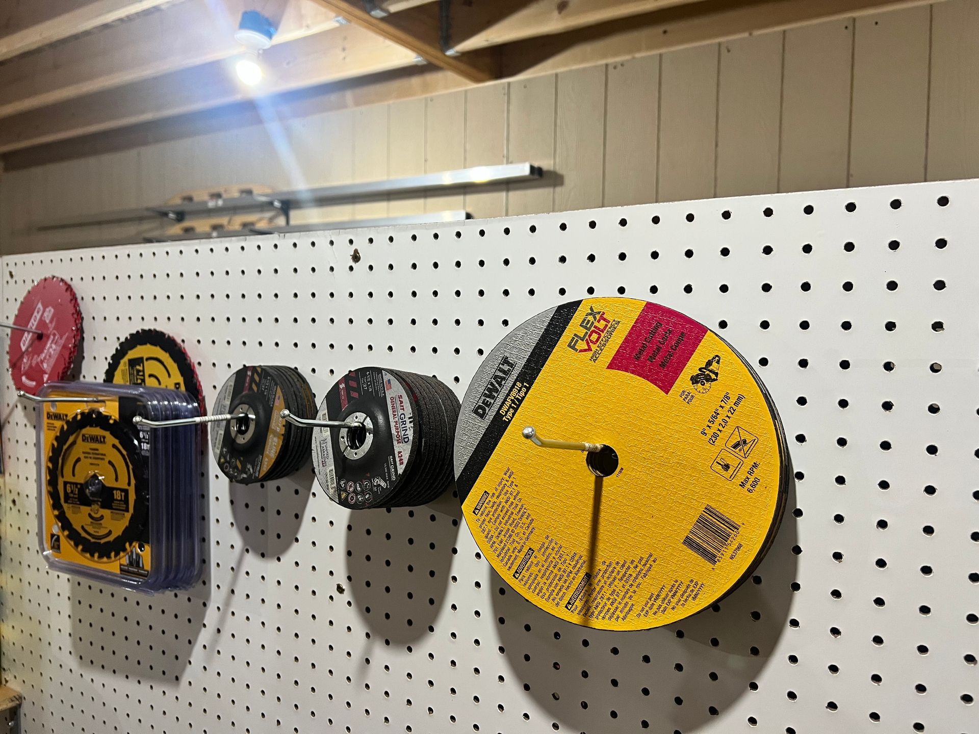 Grinding wheels and a tool holder on a white pegboard wall, lit by an overhead light.