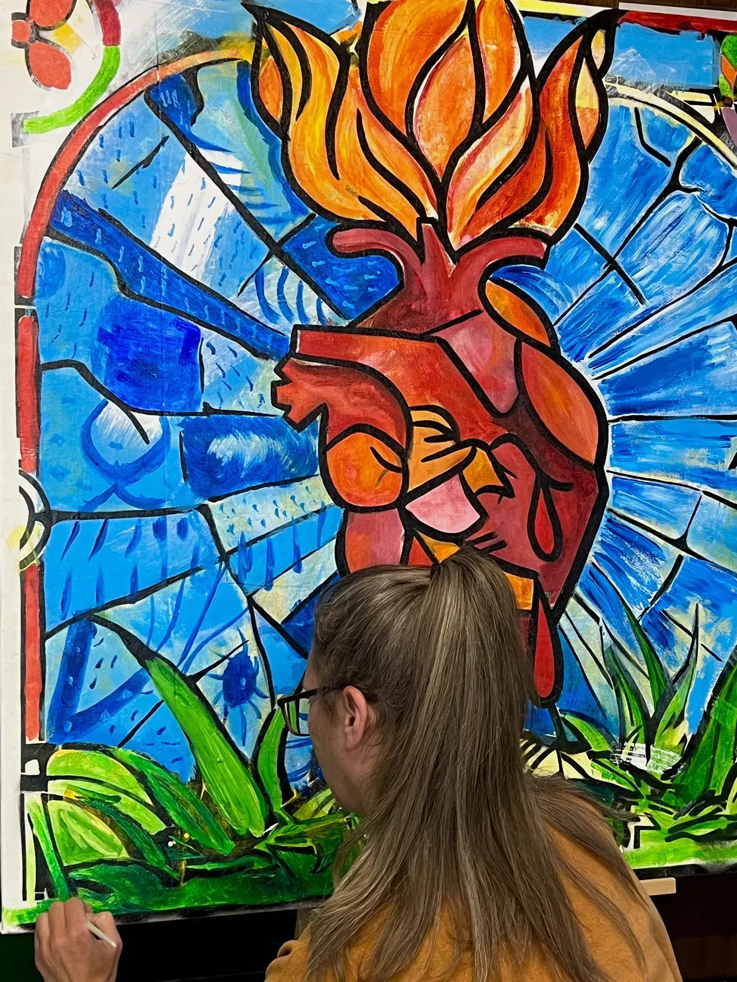 Person painting a vibrant heart on fire artwork, in front of stained-glass style backdrop.