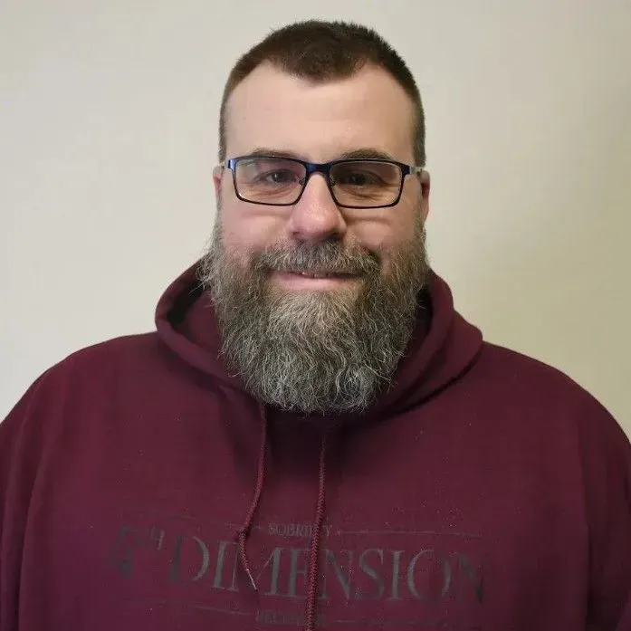 Man with a beard, glasses, and maroon hoodie, smiling, against a neutral background.