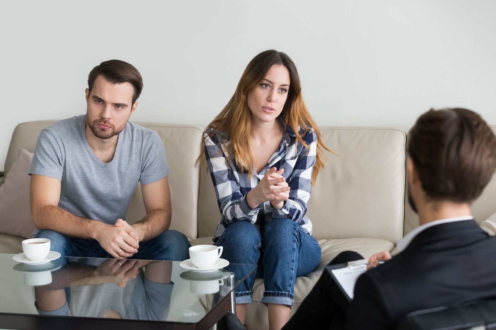 Couple and therapist in session; woman speaks, man looks concerned, all seated on couch.