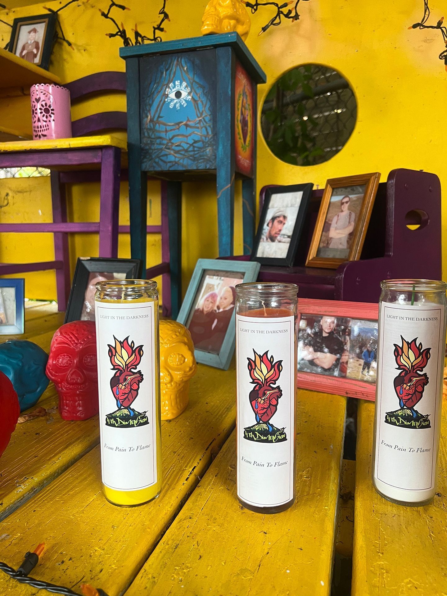 Altar with candles, photos, and decorative elements on a yellow surface, with a teal cabinet