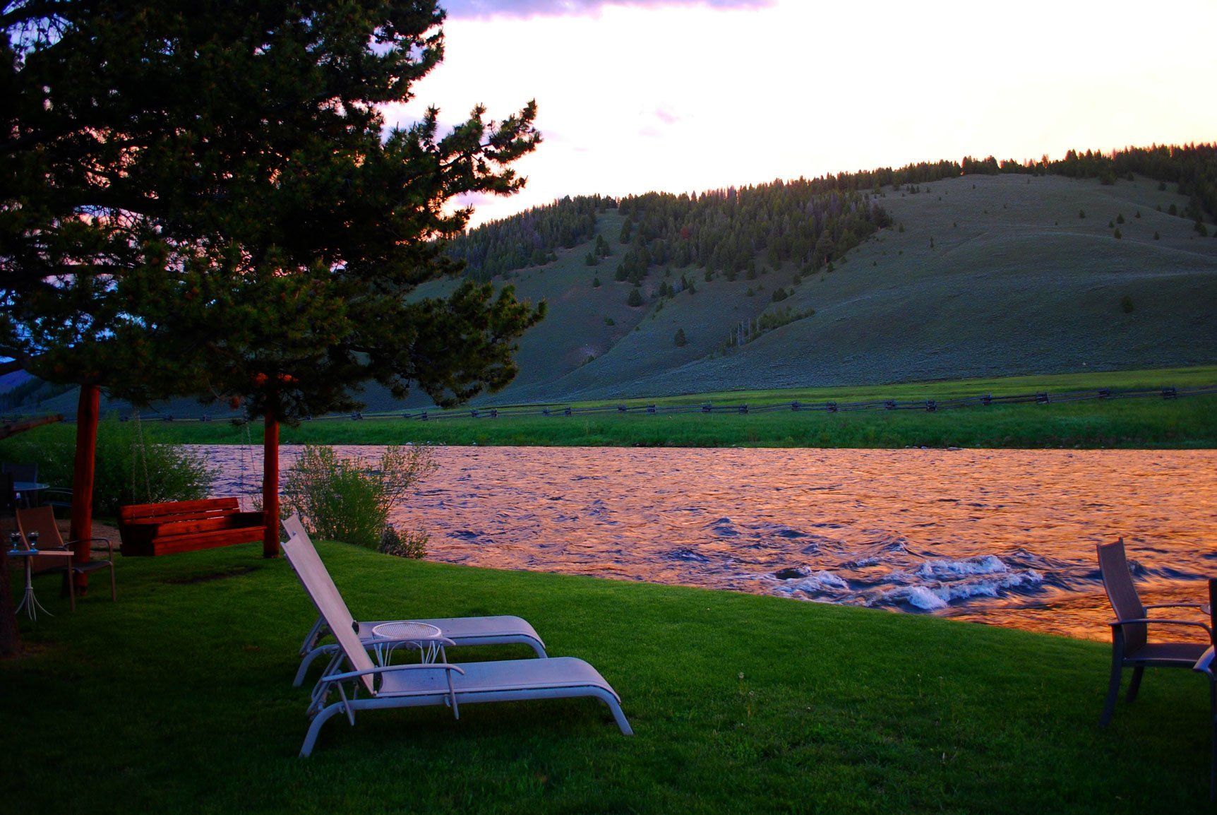 Two lounge chairs are sitting in the grass near a river