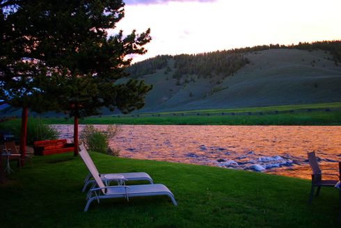 Two lounge chairs are sitting in the grass near a lake