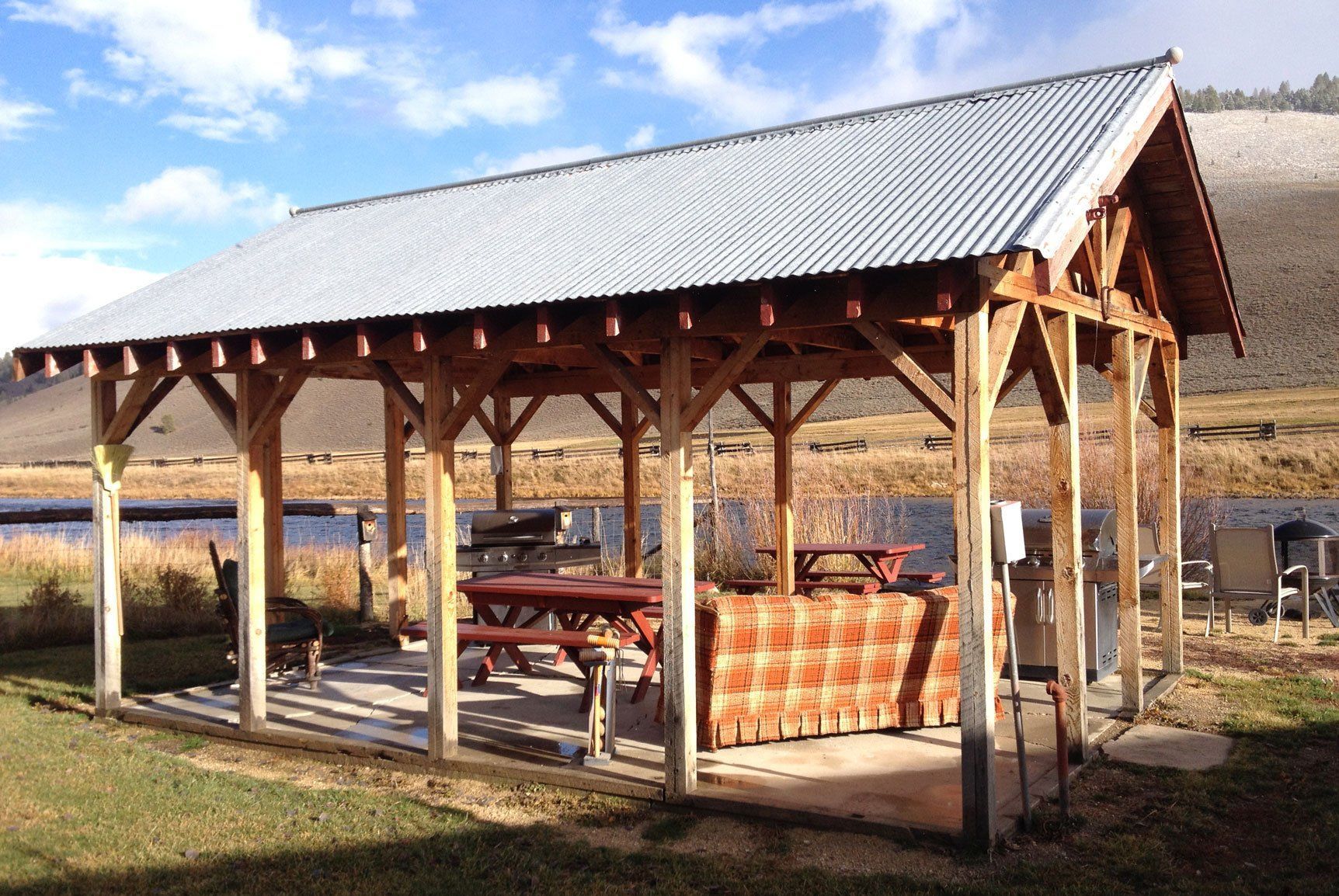 A wooden pavilion with a metal roof and picnic tables