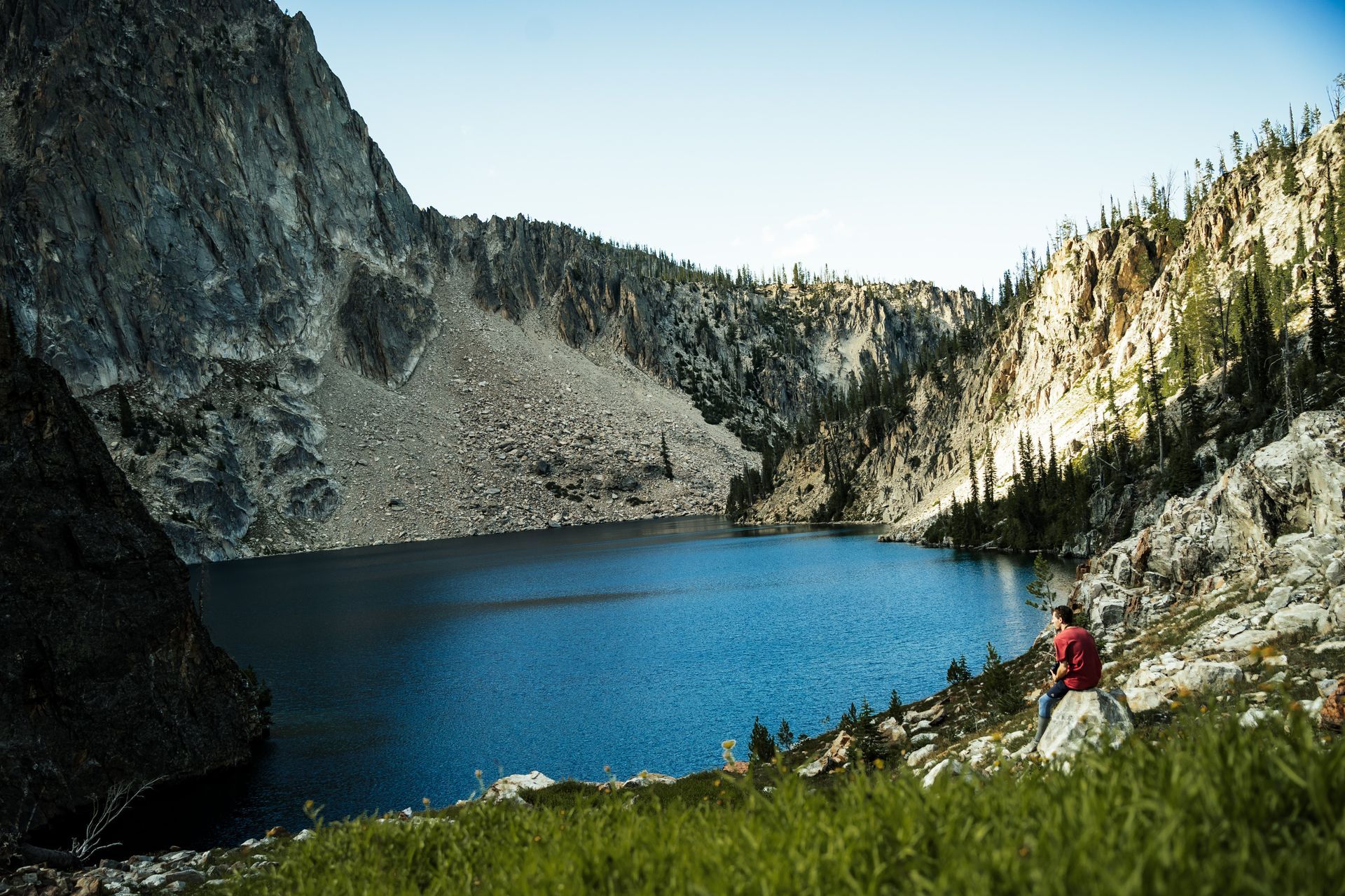 A man in a red shirt is standing next to a lake in the mountains.