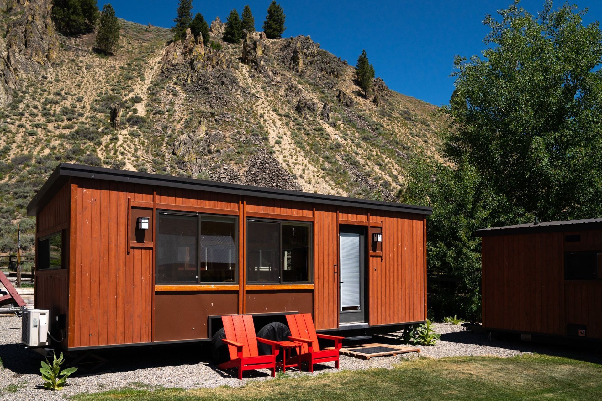 A small house on wheels with red chairs in front of it