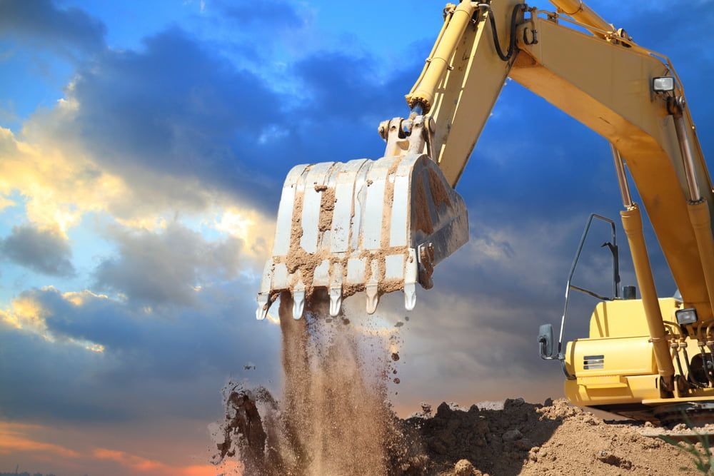 Yellow Excavator Dumping Soil Against a Cloudy Blue and Orange Sky — Dirt Werx in Nowra, NSW