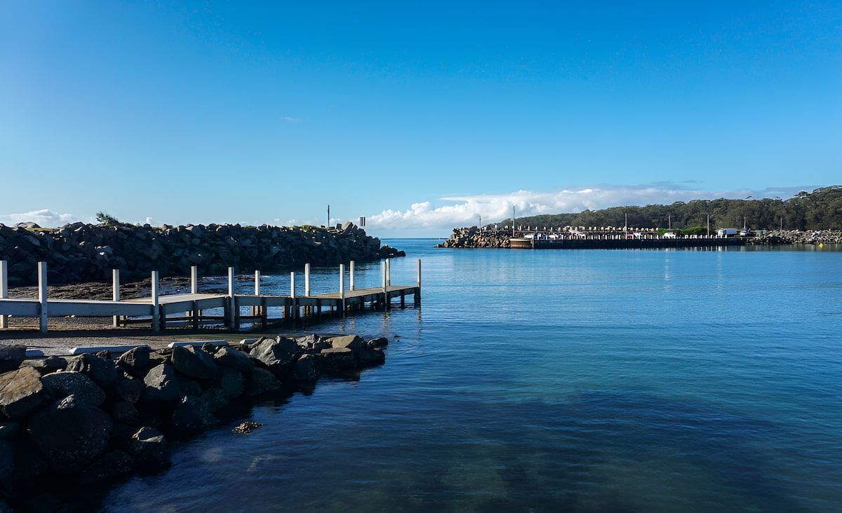 A Calm Blue Harbor With a Wooden Dock and Rocky Breakwaters — Dirt Werx in Ulladulla, NSW