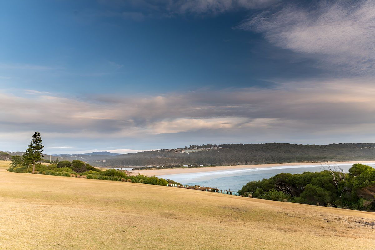 Rolling Grassy Hill Overlooking a Beach and Ocean Under a Blue Sky — Dirt Werx in Merimbula, NSW