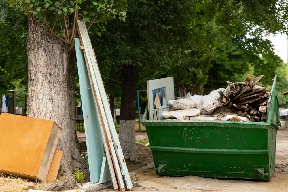 Green Dumpster Overflowing With Construction Debris in a Park Setting — Dirt Werx in Nowra, NSW