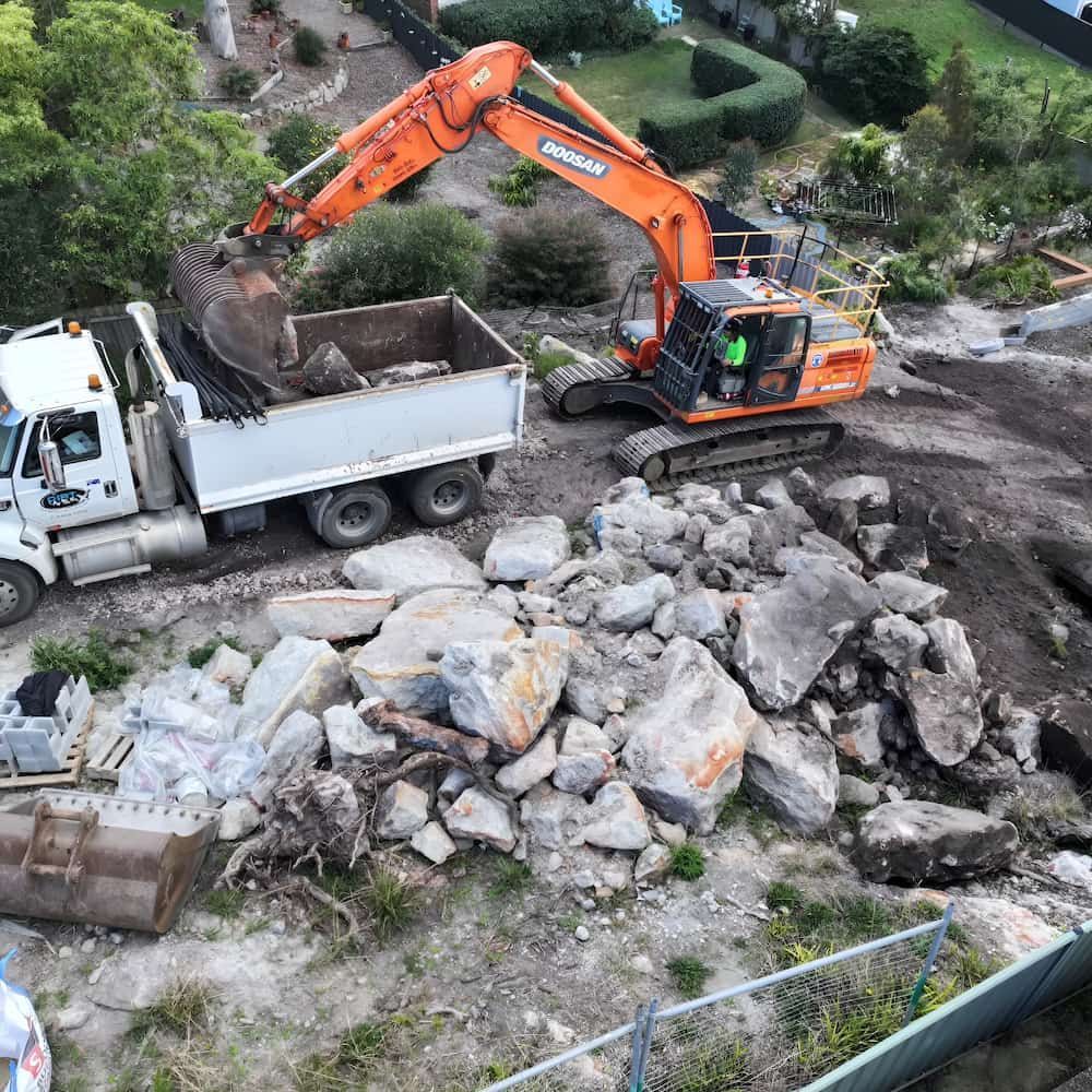 Orange Excavator Loading Large Rocks Into a Dump Truck on a Construction Site — Dirt Werx in Nowra, NSW
