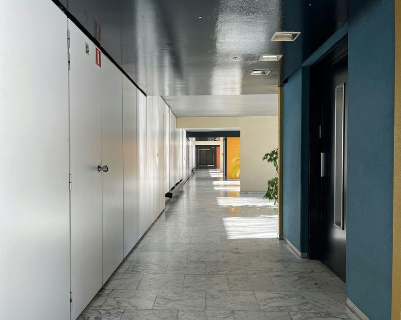 Long hallway with white lockers on the left, a blue wall on the right, and sunlight filtering through.