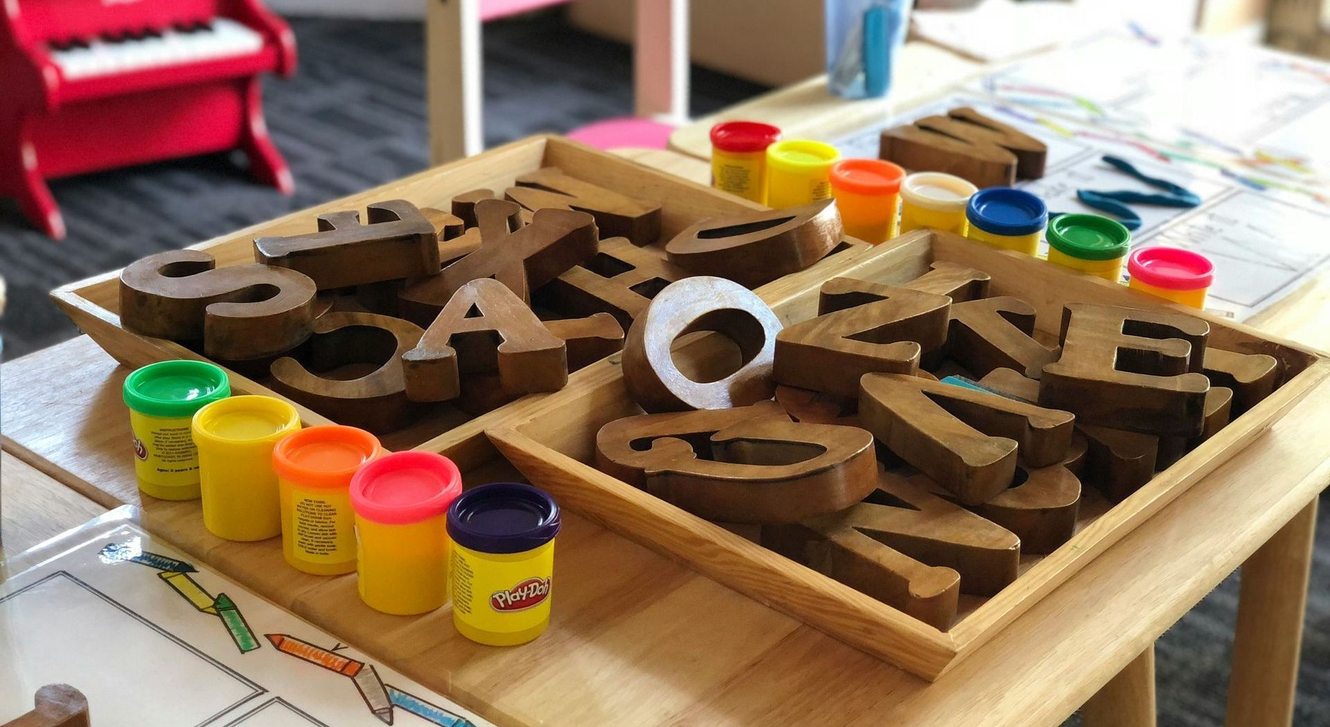 A wooden table topped with trays of play dough and cardboard letters.
