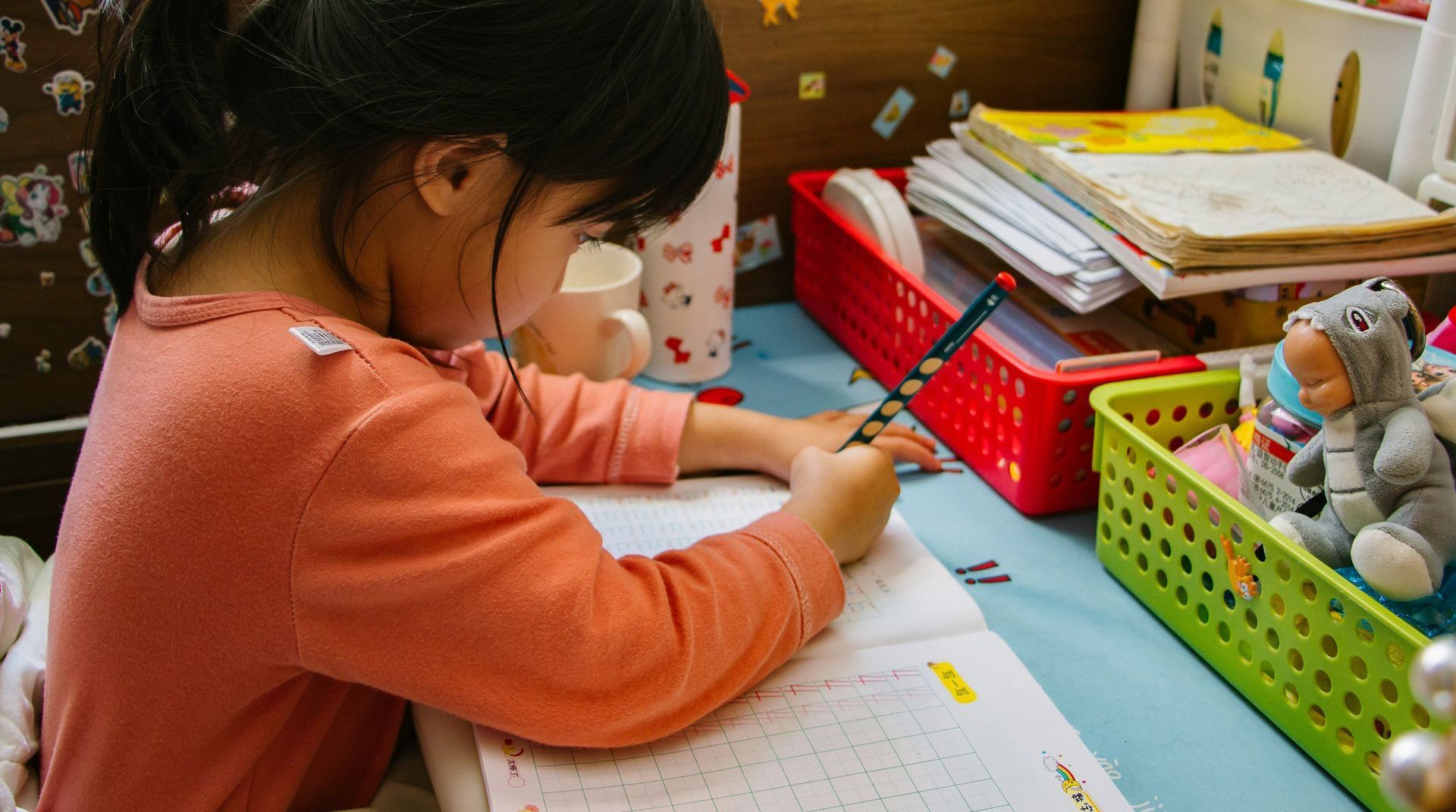 A little girl is sitting at a desk writing in a notebook.