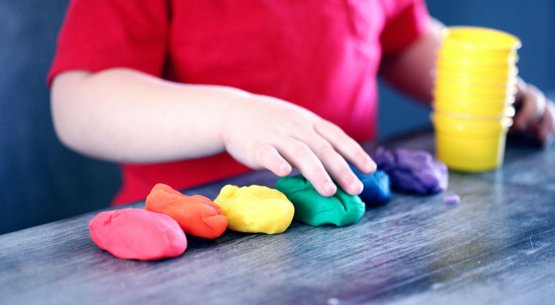 A child is playing with colored play dough on a table.