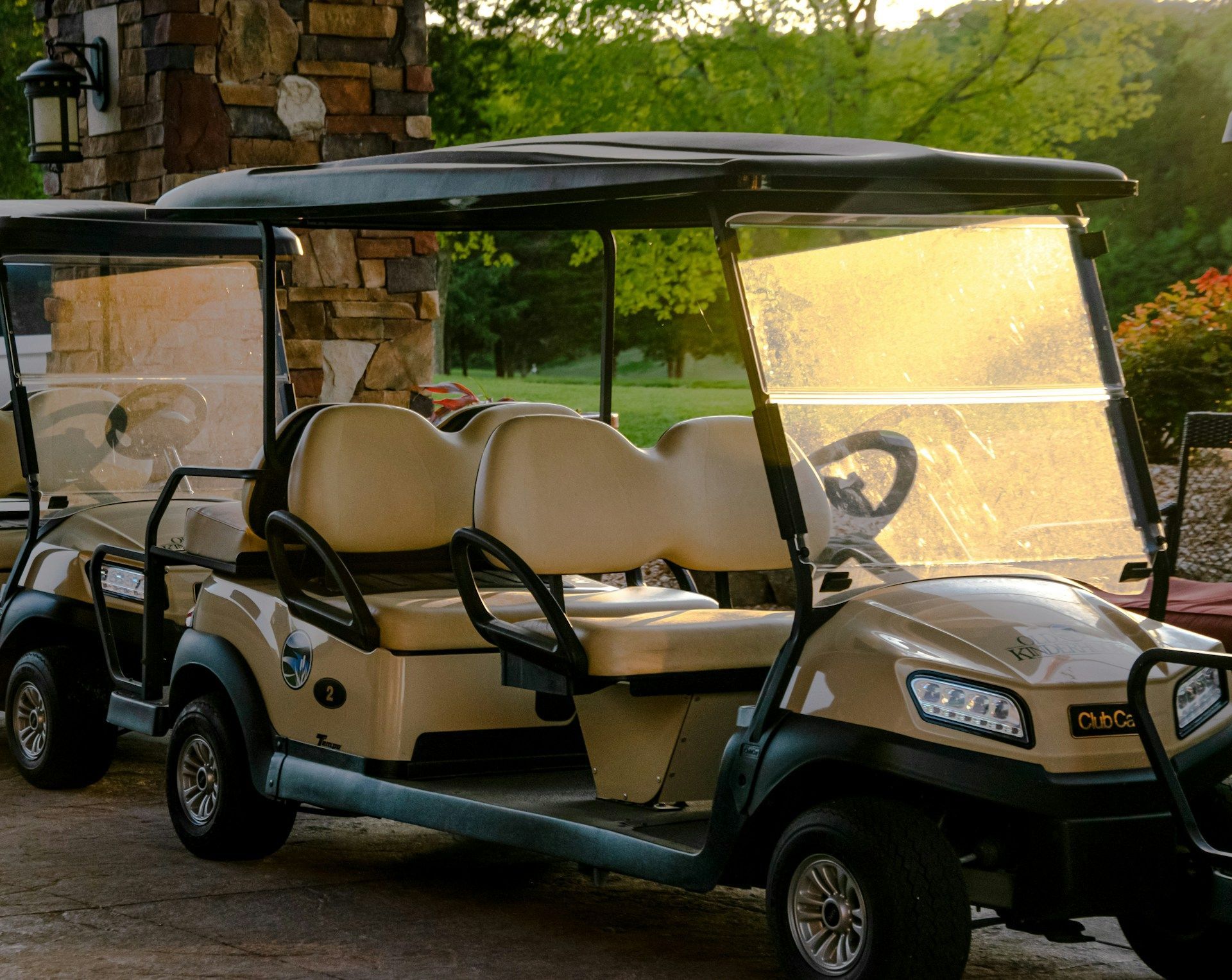 Two beige golf carts parked outdoors, with a rock structure in the background.